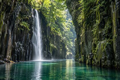 AI-generated illustration of a slender waterfall and emerald river between wooded columnar cliffs, inspired by Takachiho Gorge in Miyazaki.