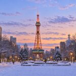 AI-generated illustration of snowy Odori Park and Sapporo TV Tower at dusk, with warm lights beneath a pastel winter sky.