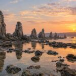 AI-generated illustration of jagged coastal rock pillars and reflective tidal pools at sunrise, inspired by Hashigui-iwa in Wakayama.