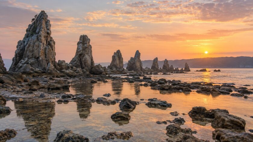 AI-generated illustration of jagged coastal rock pillars and reflective tidal pools at sunrise, inspired by Hashigui-iwa in Wakayama.