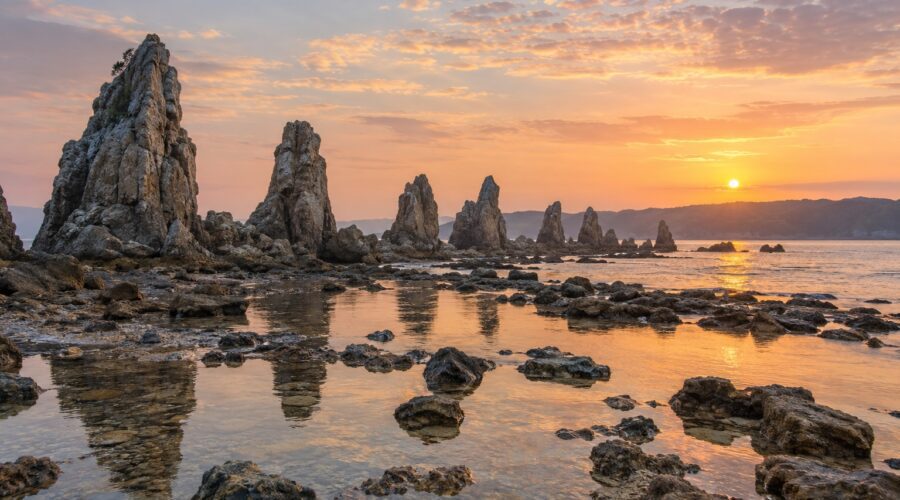 AI-generated illustration of jagged coastal rock pillars and reflective tidal pools at sunrise, inspired by Hashigui-iwa in Wakayama.